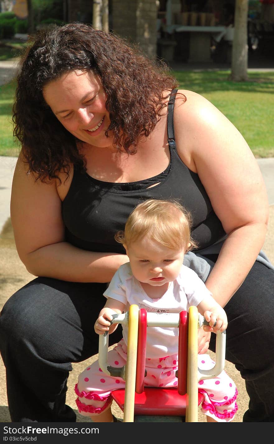 A mother and her toddler play on a tetter-totter in the park on a sunny day. A mother and her toddler play on a tetter-totter in the park on a sunny day.