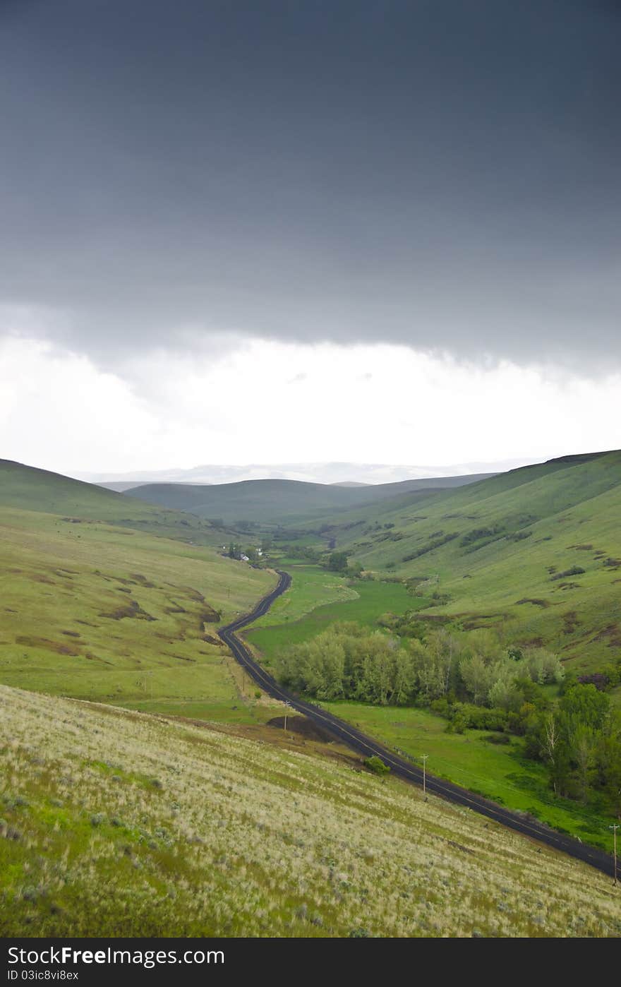 Black gravel road among grassy hills below a stormy sky. Black gravel road among grassy hills below a stormy sky