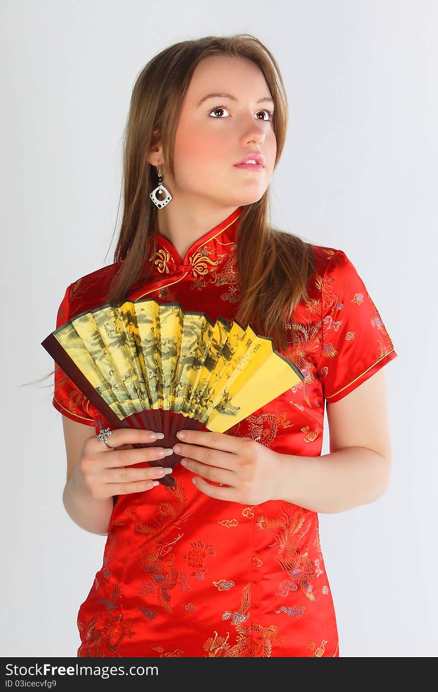 The beautiful young girl in a red Chinese dress with a yellow fan. The beautiful young girl in a red Chinese dress with a yellow fan