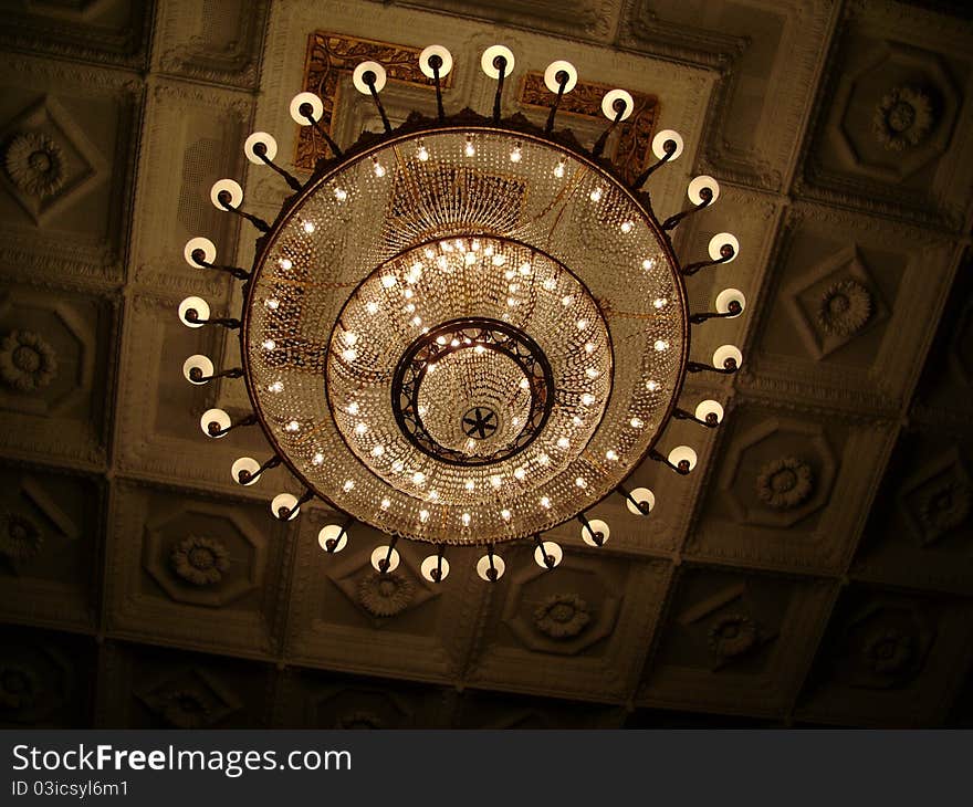 A beautiful ornate lit chandelier reflecting against the ceiling. A beautiful ornate lit chandelier reflecting against the ceiling