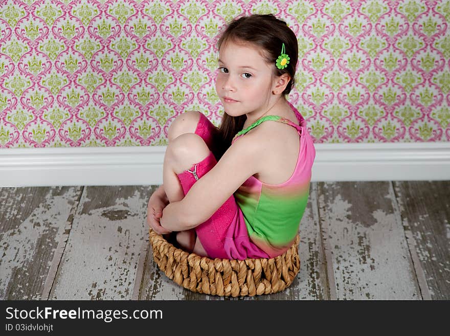 Cute girl sitting in basket on the old-fashion floor. Cute girl sitting in basket on the old-fashion floor