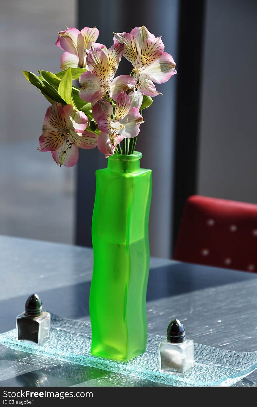 A flower arrangement in a green vase on a table with salt and pepper shakers tasefully decorated for lunch or dinner. A flower arrangement in a green vase on a table with salt and pepper shakers tasefully decorated for lunch or dinner.