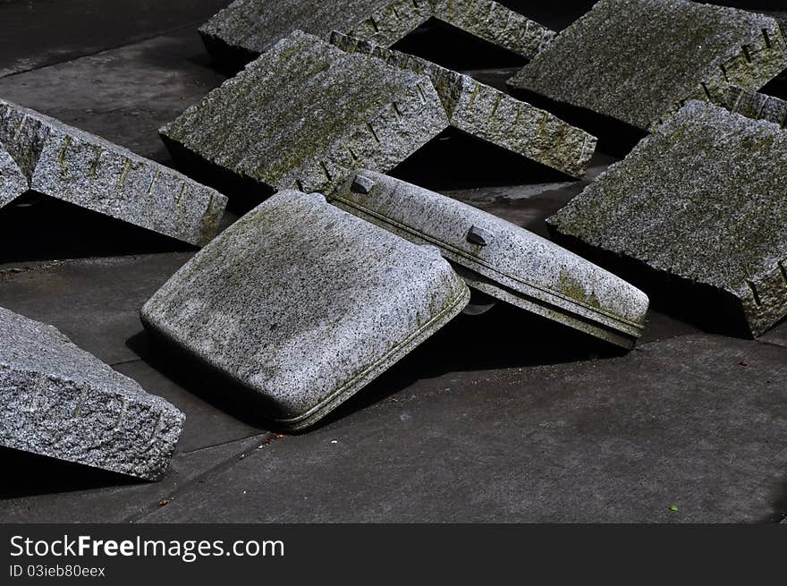 A granite rock upside down suitcase sitting on a sidewalk with slabs of granite rocks. A granite rock upside down suitcase sitting on a sidewalk with slabs of granite rocks.