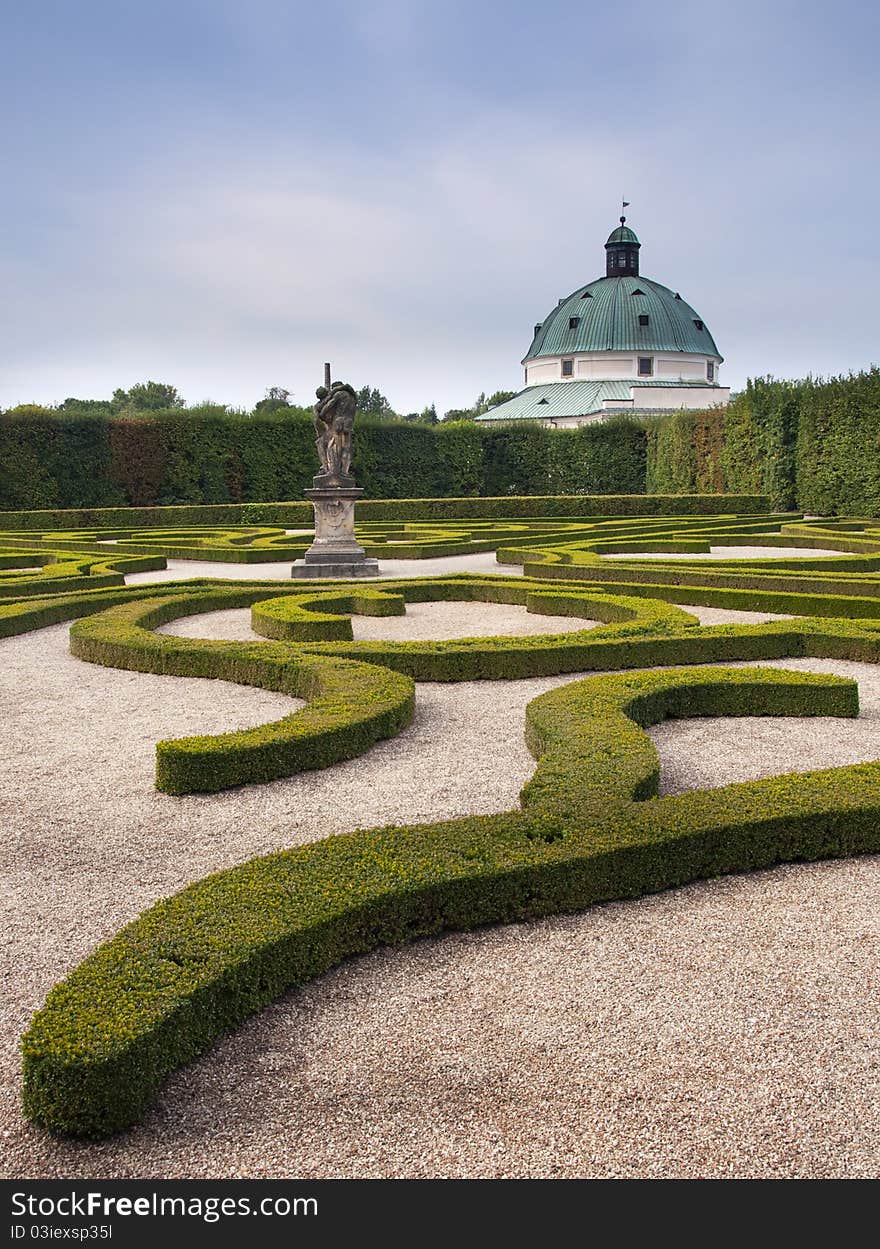 Formal garden of ornamental shaped plants with a statue and historical building in the background; UNESCO side, Kromeriz, The Czech Republic