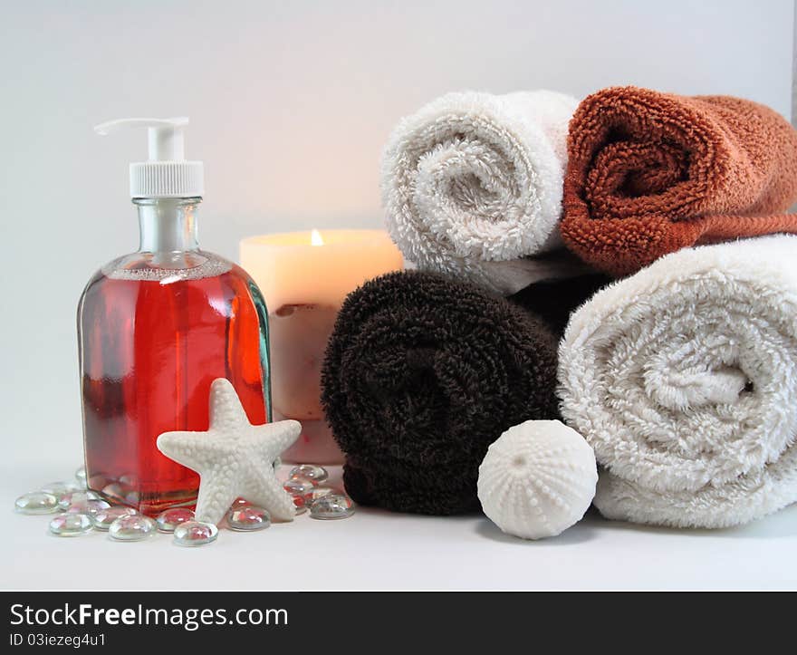 White and colored towels with orange liquid soap, lit candle, and white solid soaps in shapes. White and colored towels with orange liquid soap, lit candle, and white solid soaps in shapes