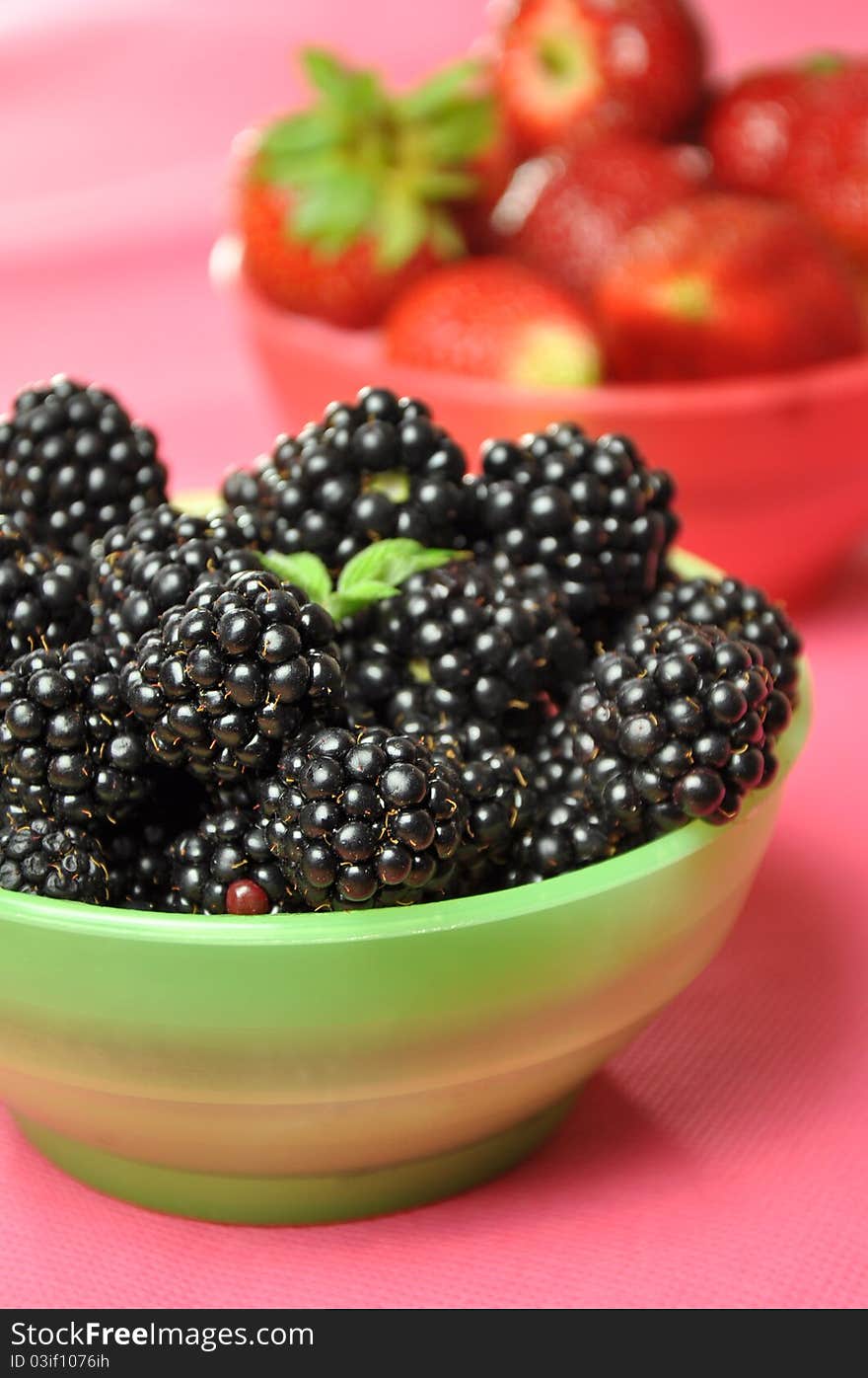 Blackberries and strawberries in colorful bowls on a pink background.