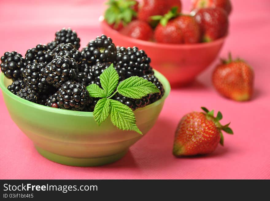 Blackberries and strawberries in colorful bowls on a pink background.