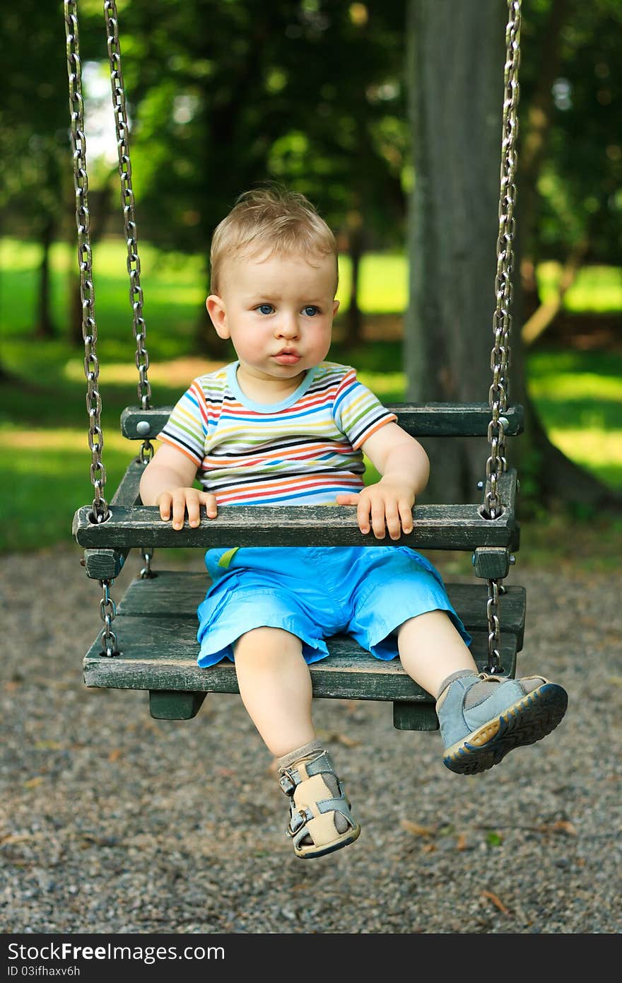 A handsome little boy swinging at the playground in the park