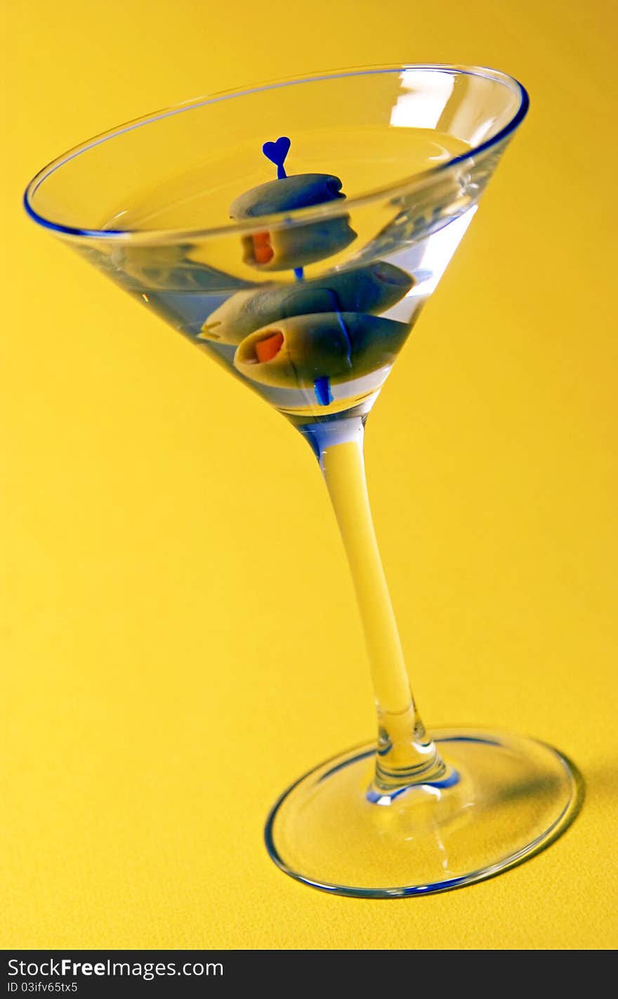 Martini with olive on yellow background