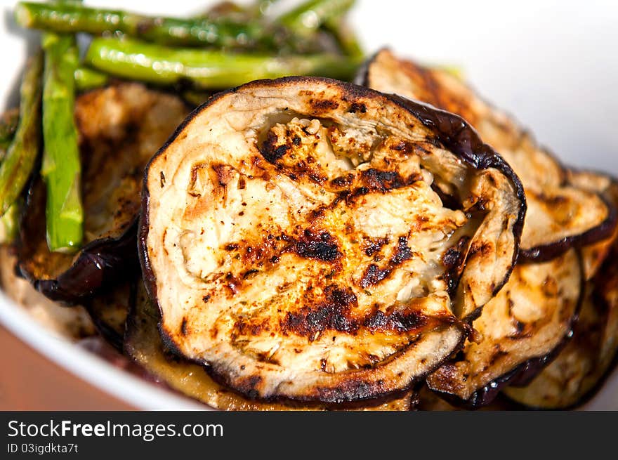 Grilled eggplants and asparagus in a white bowl.