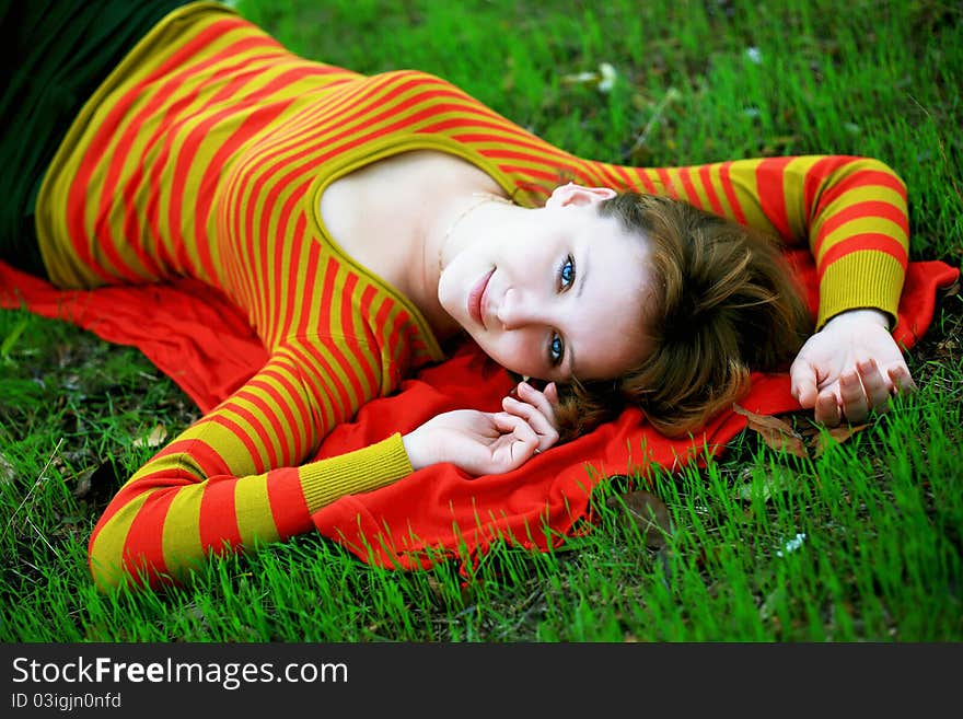 Portrait of a girl in a bright colored striped sweater lying on the grass. Portrait of a girl in a bright colored striped sweater lying on the grass