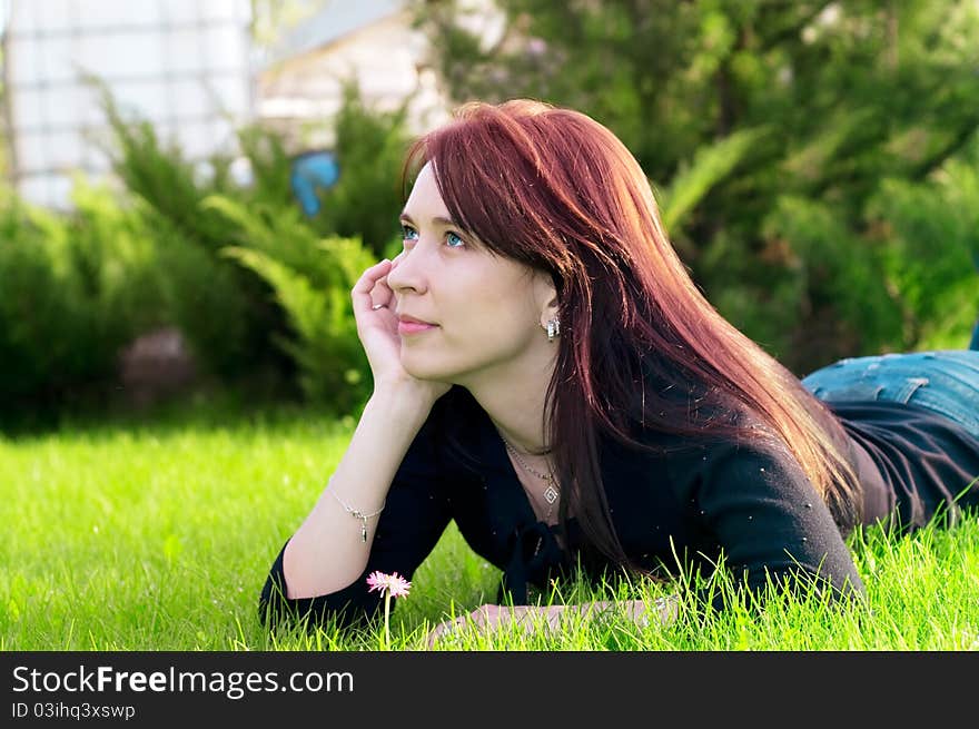 Portrait of a young pretty woman lying on green grass in the meadow