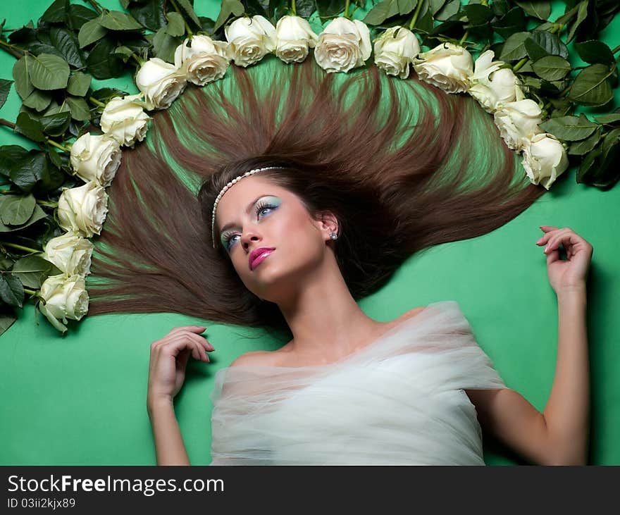 Young girl lay among the flowers of roses on a green background