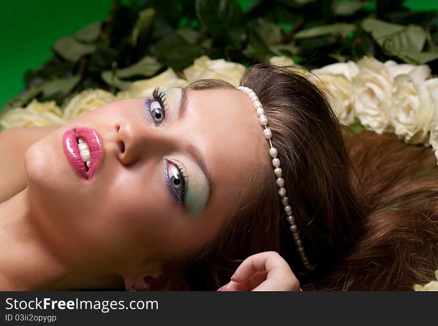 Young girl lay among the flowers of roses on a green background