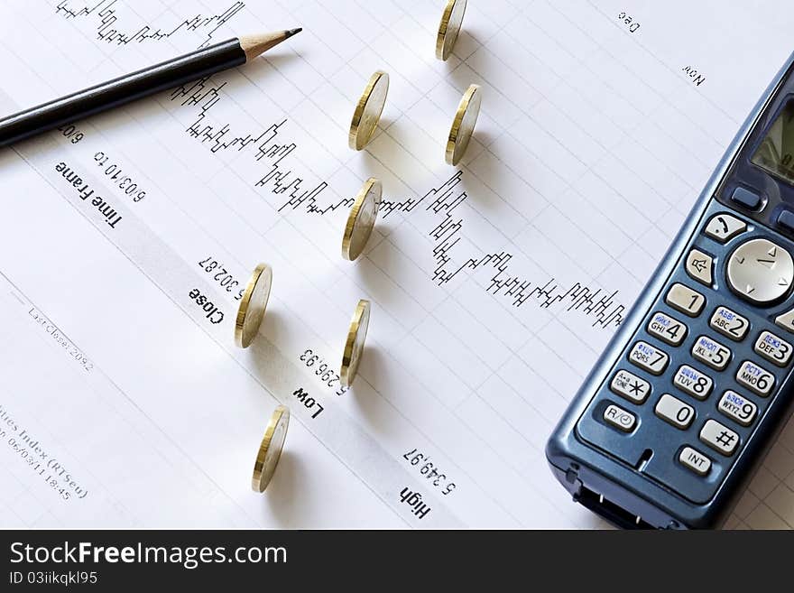 Stock chart with a pencil, phone, and coins on the table. Stock chart with a pencil, phone, and coins on the table