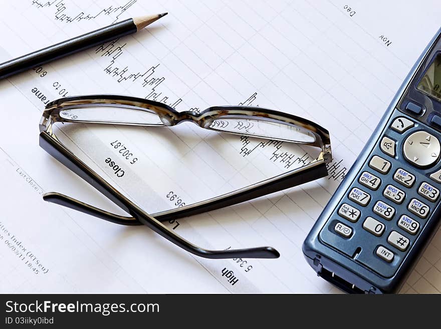 Stock chart with a pencil, phone and glasses on the table