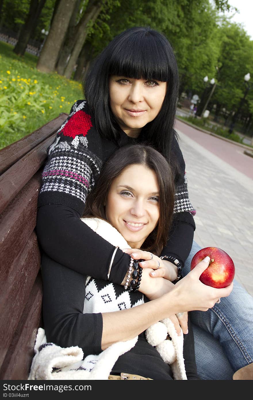 Mother and daughter in a park sitting on a wooden bench eating apples