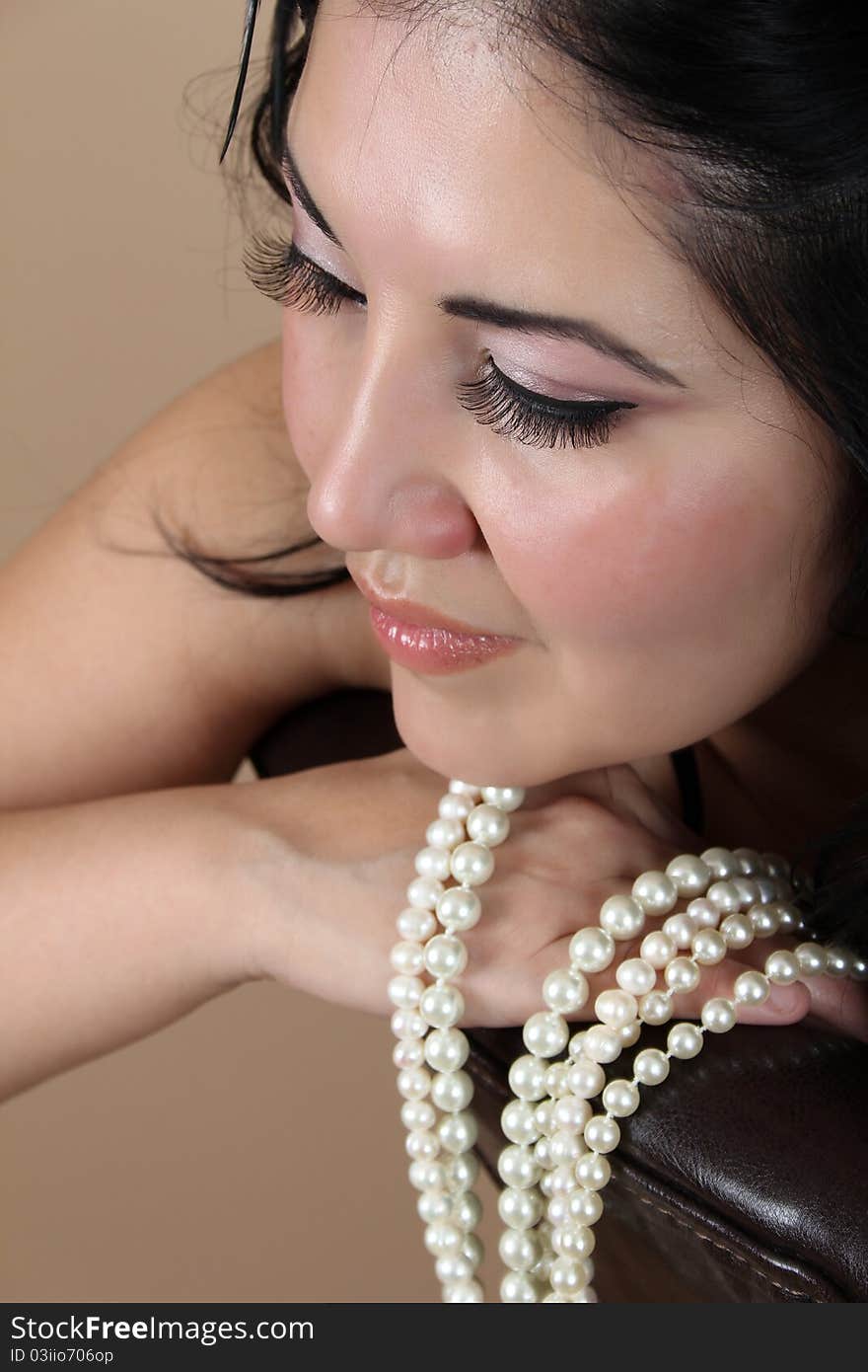 Beautiful brunette female leaning on chair back with pearls. Beautiful brunette female leaning on chair back with pearls