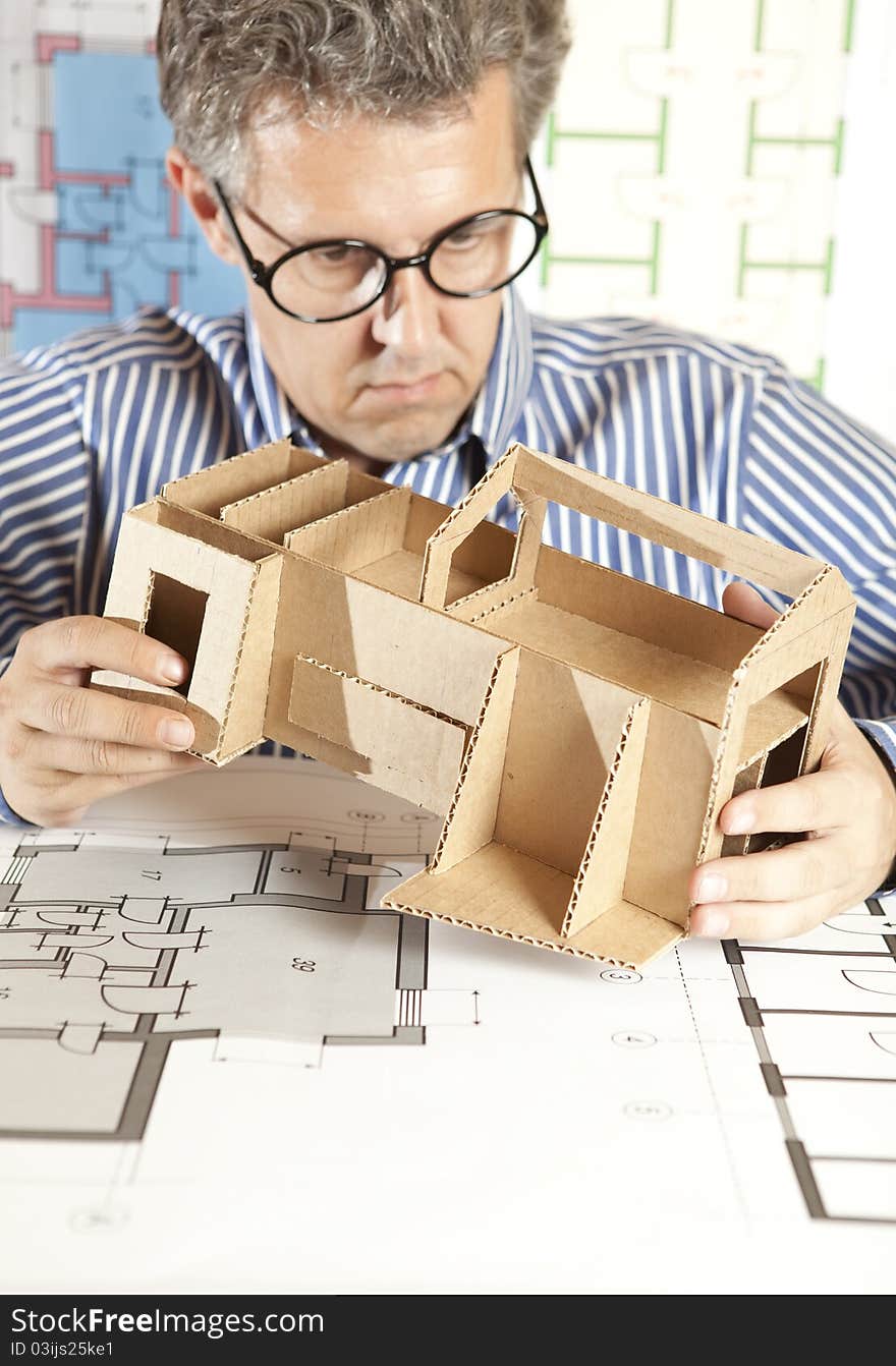 A male architect working on blueprints with a model house