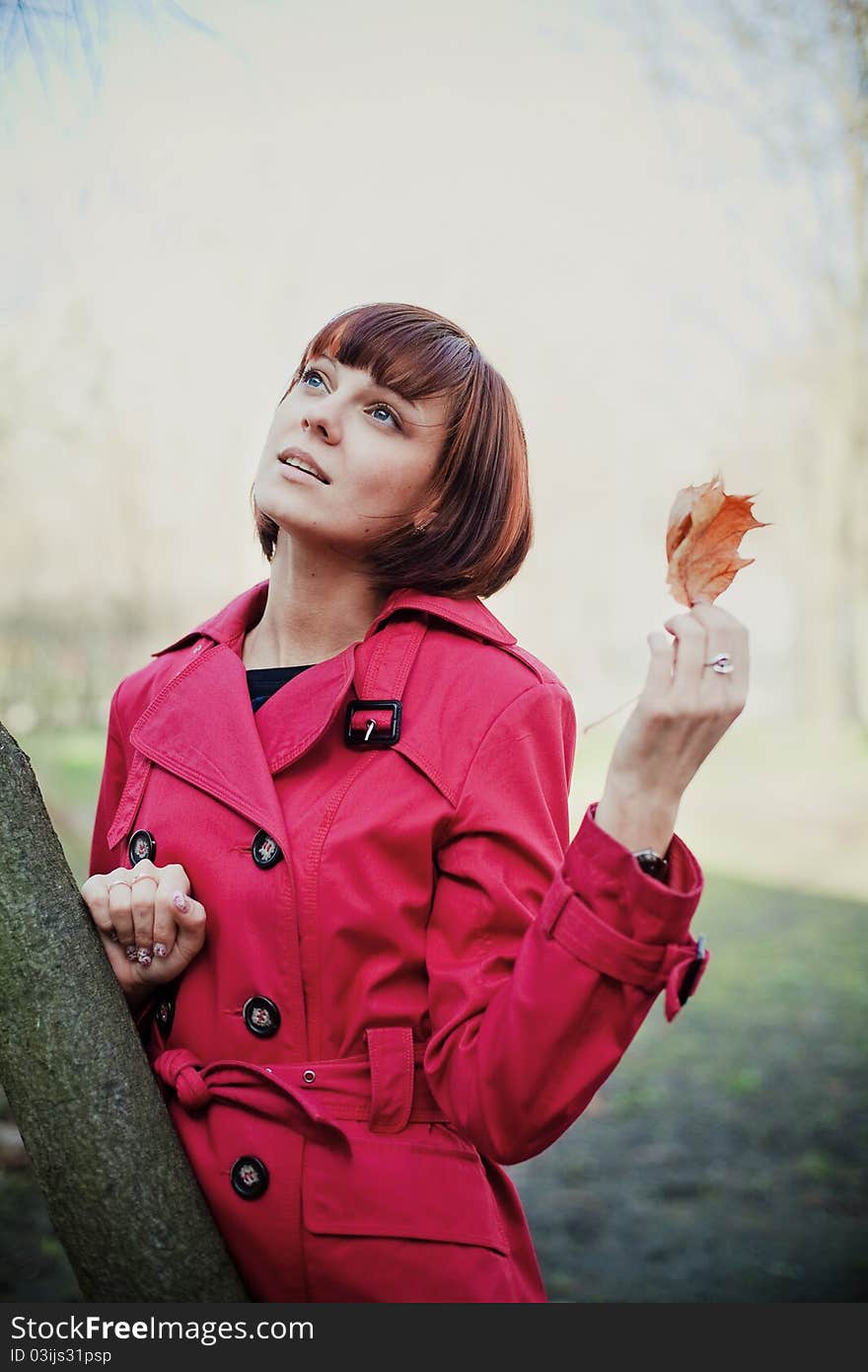 Young beautiful woman in red coat holding orange dry leaf and looking up. Young beautiful woman in red coat holding orange dry leaf and looking up