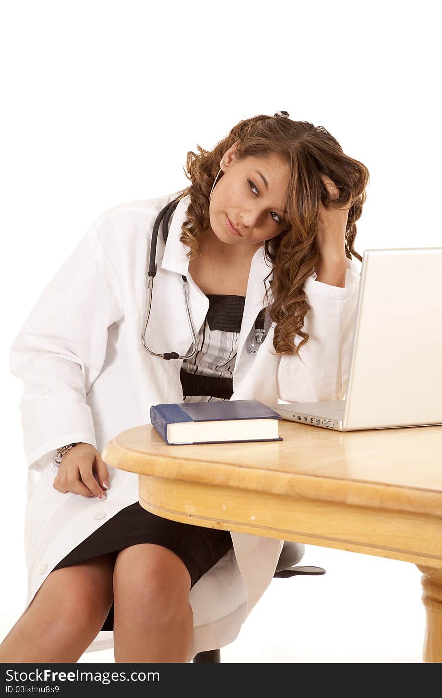 A doctor is working on finding answers to a problem in a book and on the laptop. She is stressed and tired. A doctor is working on finding answers to a problem in a book and on the laptop. She is stressed and tired.