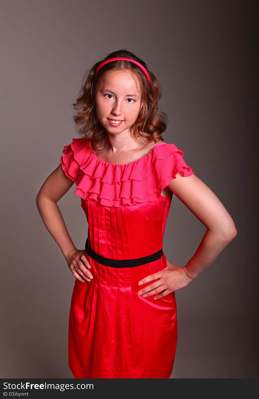 Beautiful woman in beautiful red dress is standing on a dark background in studio. Beautiful woman in beautiful red dress is standing on a dark background in studio.