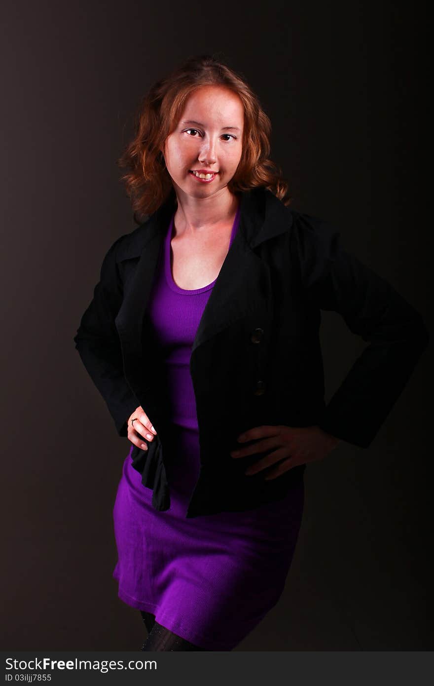 Business woman in beautiful purple sporty dress and a jacket is standing on a dark background. Business woman in beautiful purple sporty dress and a jacket is standing on a dark background.