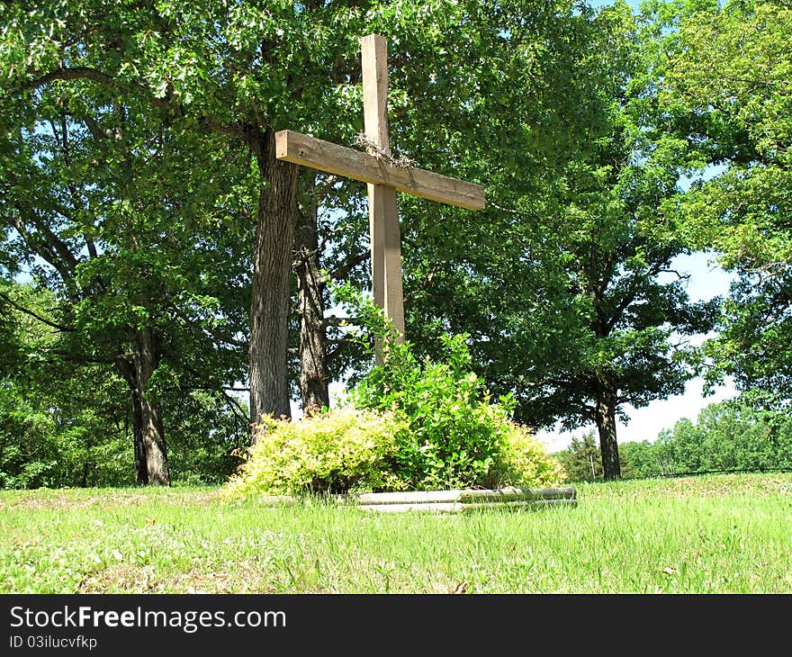 Wooden cross in a churchyard with a crown of thorns surrounded by bushes. Wooden cross in a churchyard with a crown of thorns surrounded by bushes