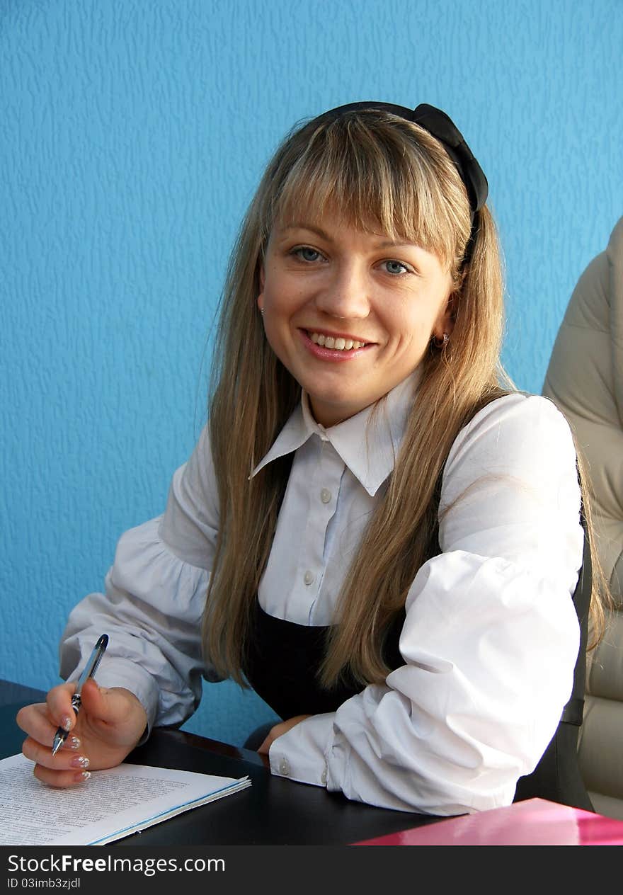 Young woman with long hair and a white shirt sitting in the office behind a desk. Young woman with long hair and a white shirt sitting in the office behind a desk