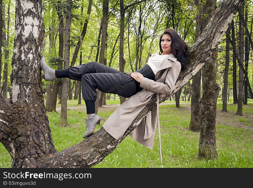 Thoughtful beautiful long haired brunette, is resting in a park in a tree. Thoughtful beautiful long haired brunette, is resting in a park in a tree