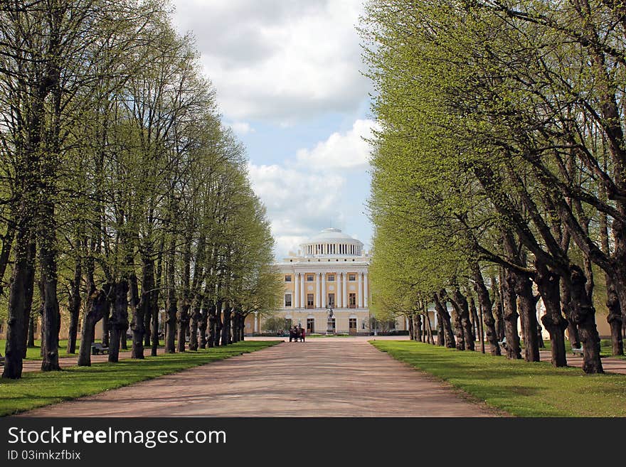 Ancient palace in the old park. Cloudy day at the beginning of spring under the shelter of long alley of linden trees.