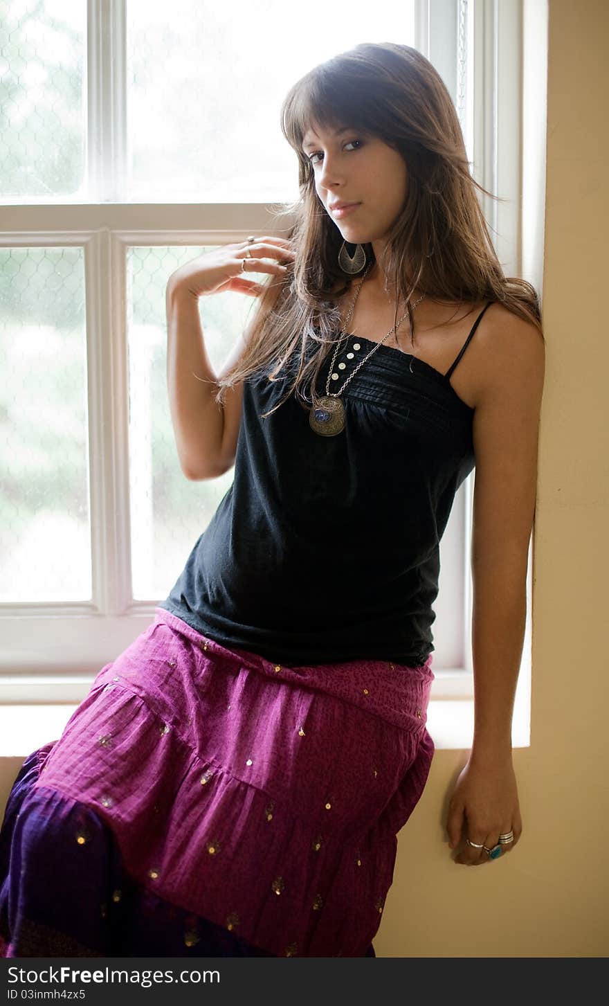 A portrait of a young woman sitting on a windowsill and smiling at the viewer. A portrait of a young woman sitting on a windowsill and smiling at the viewer