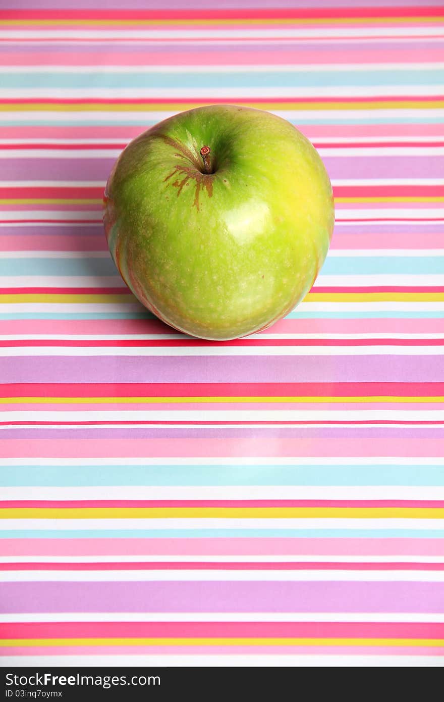 A bright green apple sits alone against a reflective stripy background. A bright green apple sits alone against a reflective stripy background