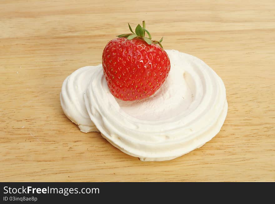 Single ripe strawberry in a meringue nest on a wooden food preparation board. Single ripe strawberry in a meringue nest on a wooden food preparation board