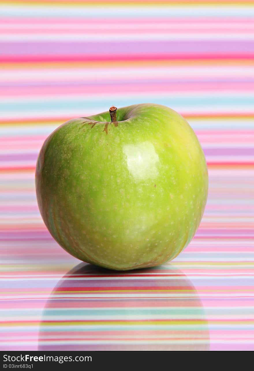 A bright green apple sits alone against a reflective stripy background. A bright green apple sits alone against a reflective stripy background