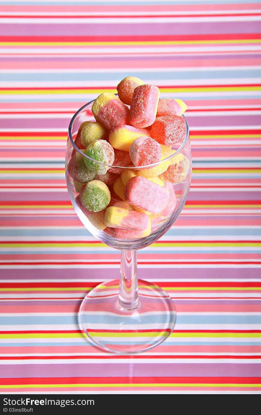 A large glass full of multi coloured tasty sugary sweets against a coloured stripy background. A large glass full of multi coloured tasty sugary sweets against a coloured stripy background.