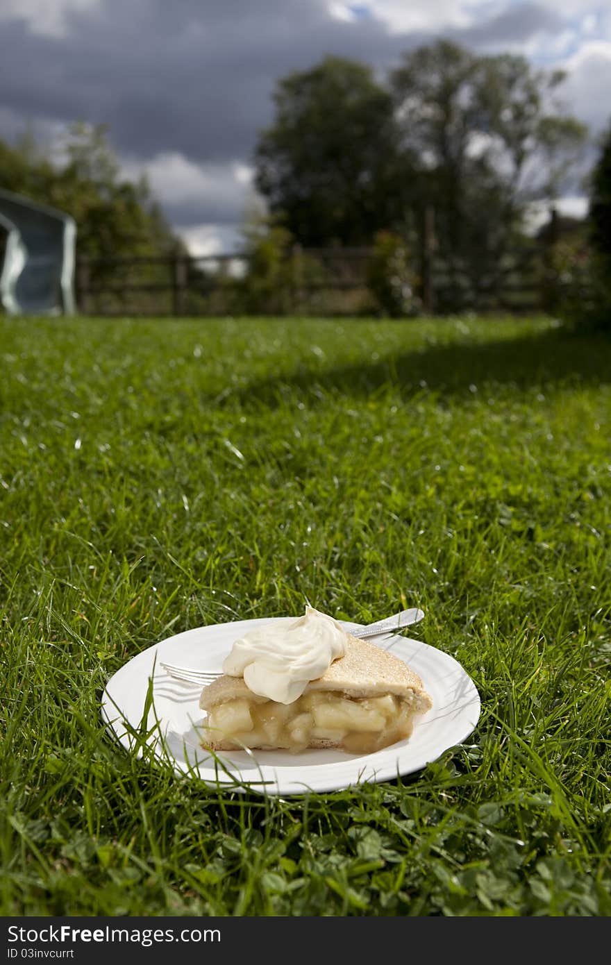 Apple pie and cream served on a plate and placed on a garden lawn