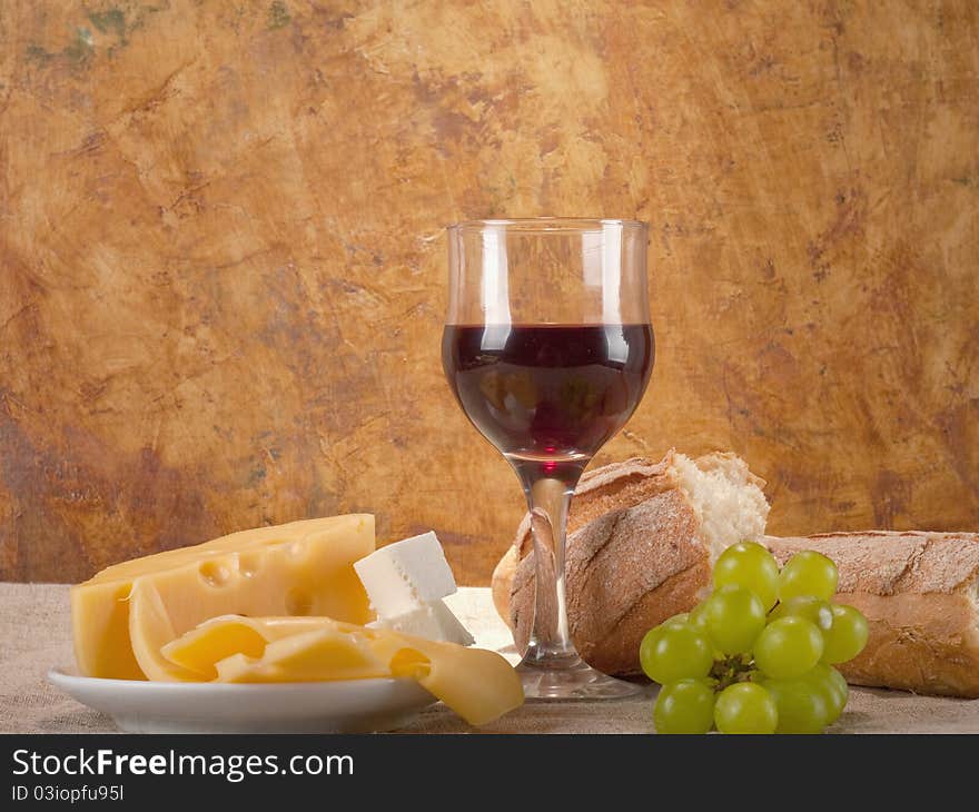 Red wine, assorted cheeses, bread and grapes in a still life setup.