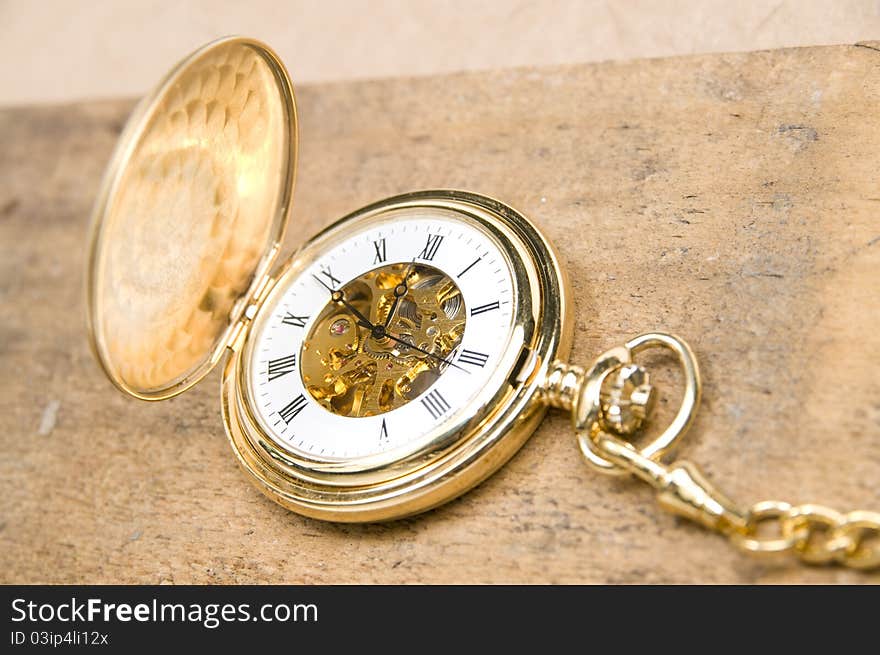 The golden pocket watch on the rough wood board. The golden pocket watch on the rough wood board