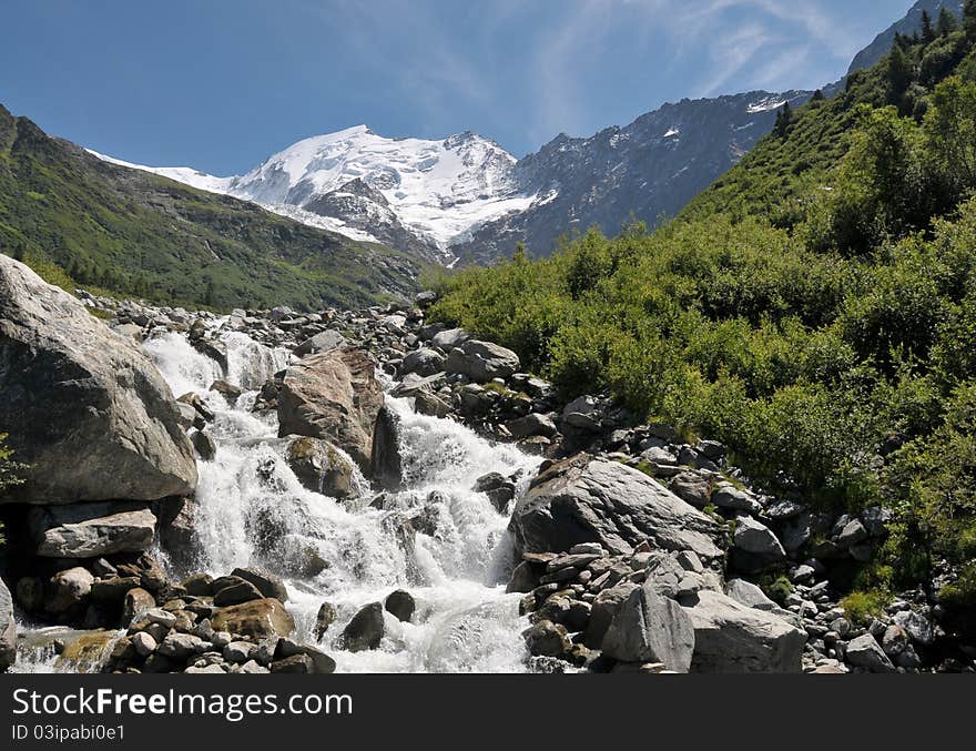 View of high mountains with snow and rapid stream.