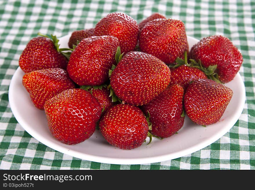 A lot of big ripe strawberries on a white plate, is on the table with green cloth. A lot of big ripe strawberries on a white plate, is on the table with green cloth