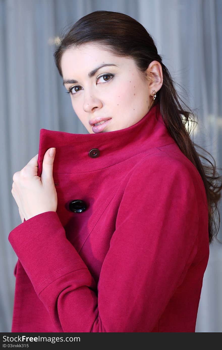 Side shot, yound woman with brown hair in venous coat by blue background. Side shot, yound woman with brown hair in venous coat by blue background