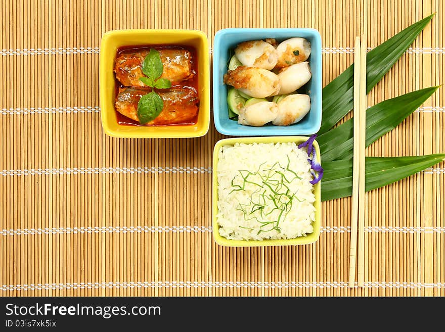 Cooked rice with fish in sauces and fried cuttlefish on bamboo pad. Cooked rice with fish in sauces and fried cuttlefish on bamboo pad