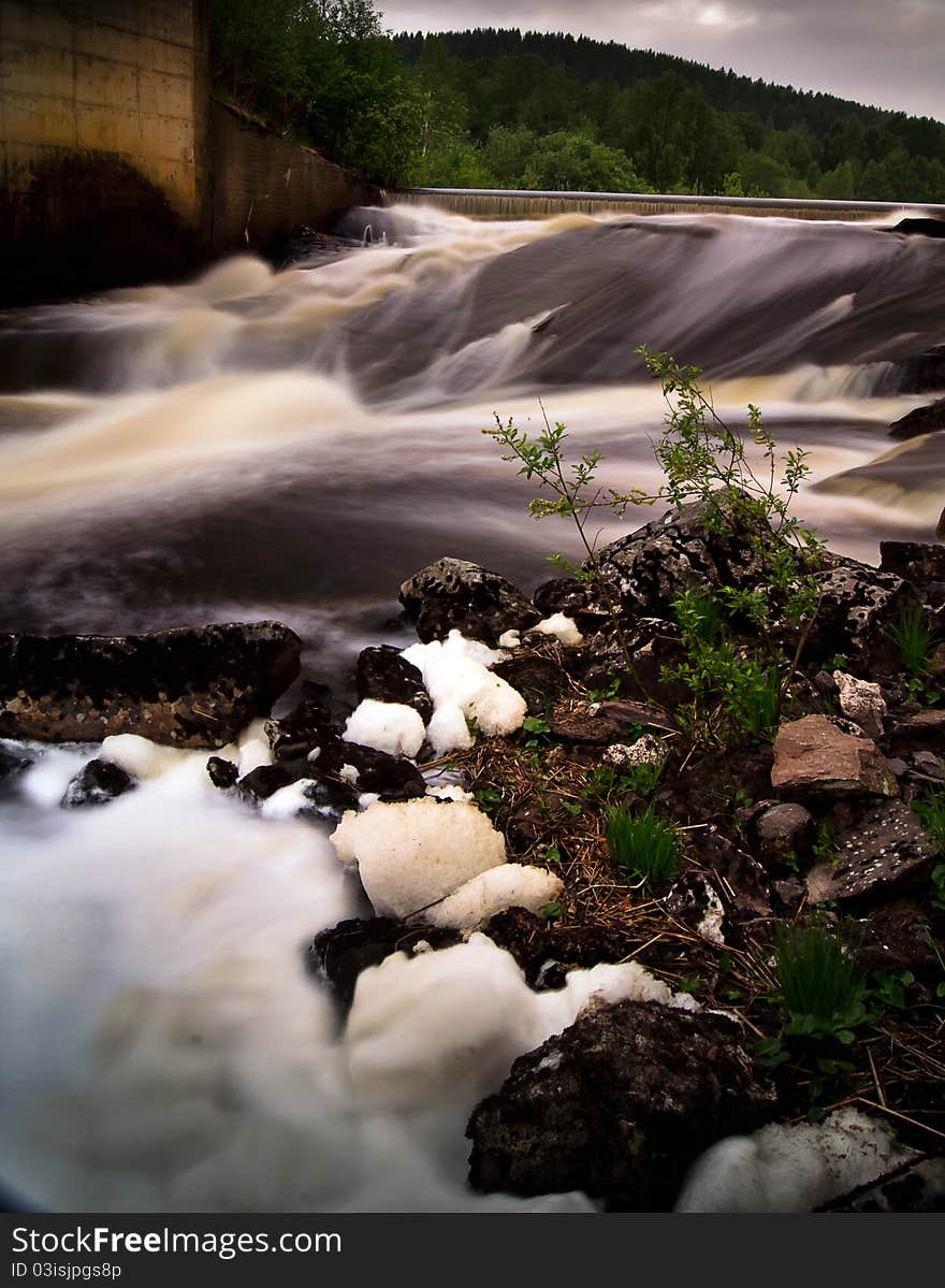 A river with a little waterfall. Foam from the water in ther foreground. A river with a little waterfall. Foam from the water in ther foreground.