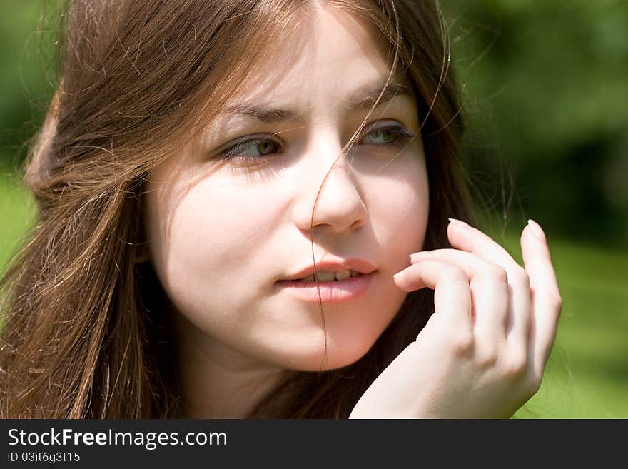 Portrait of young woman with clear skin is touching her face by hand in park on green background. Portrait of young woman with clear skin is touching her face by hand in park on green background