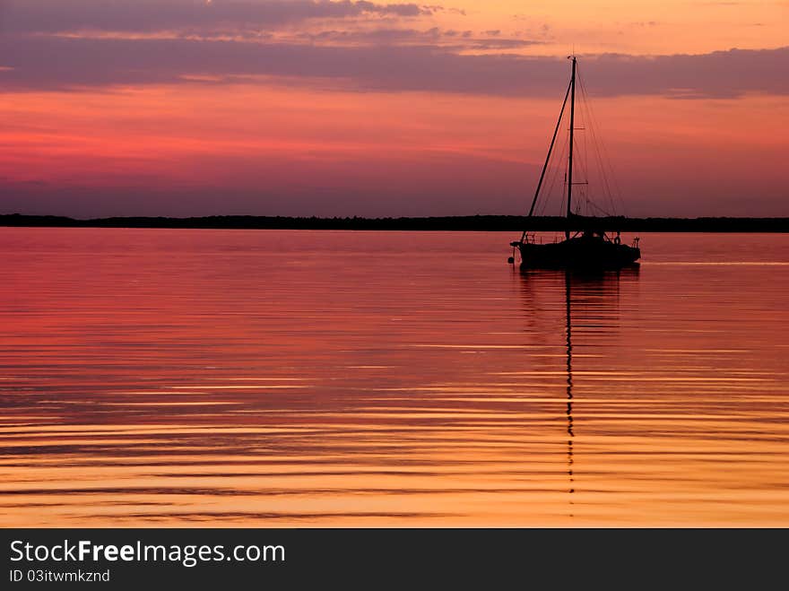 Silhouette of a sailboat on a calm golden lake at sunset. Silhouette of a sailboat on a calm golden lake at sunset