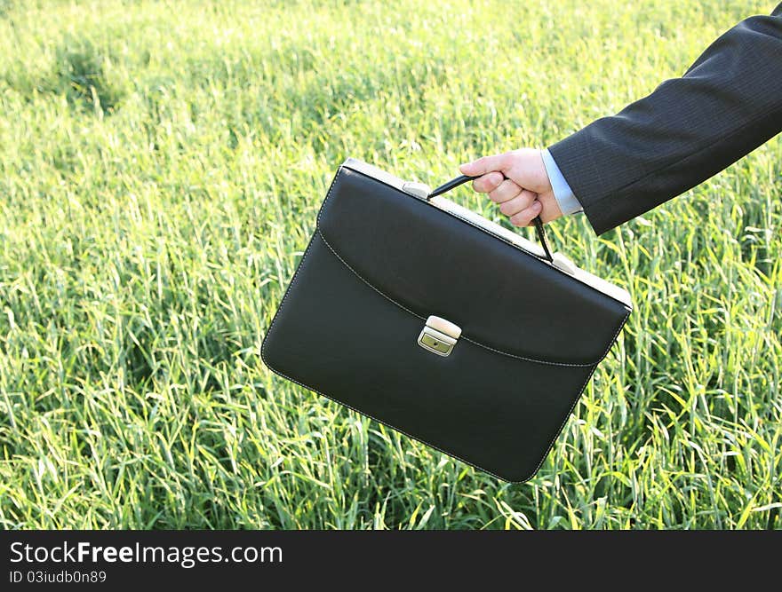 Hand businessman with briefcase against the backdrop of the field. Hand businessman with briefcase against the backdrop of the field