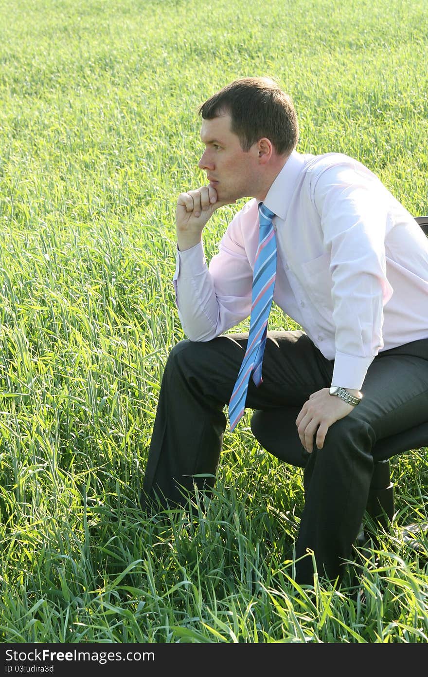 Pensive businessman sitting on meadow. Pensive businessman sitting on meadow