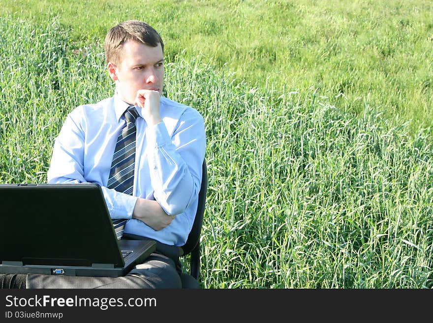 Pensive businessman in the field with laptop. Pensive businessman in the field with laptop