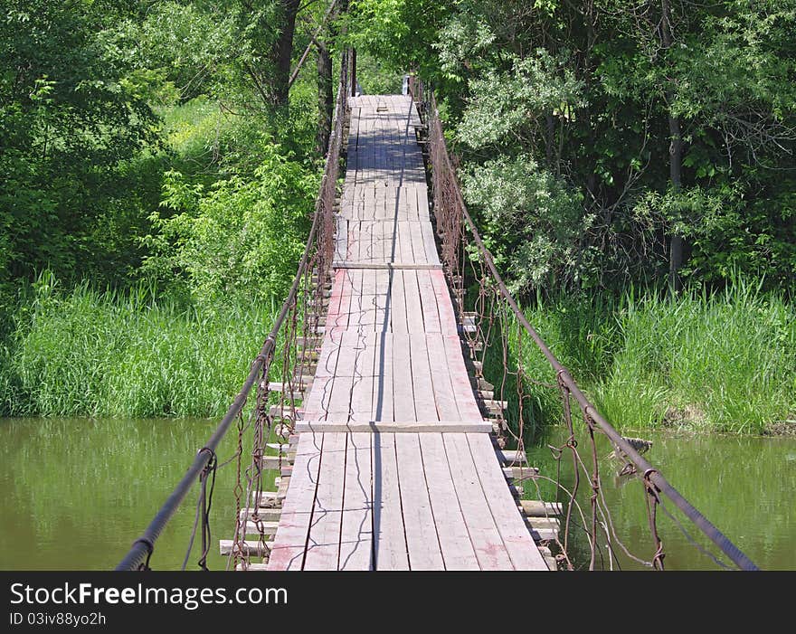 Old suspension walk bridge across river in forest